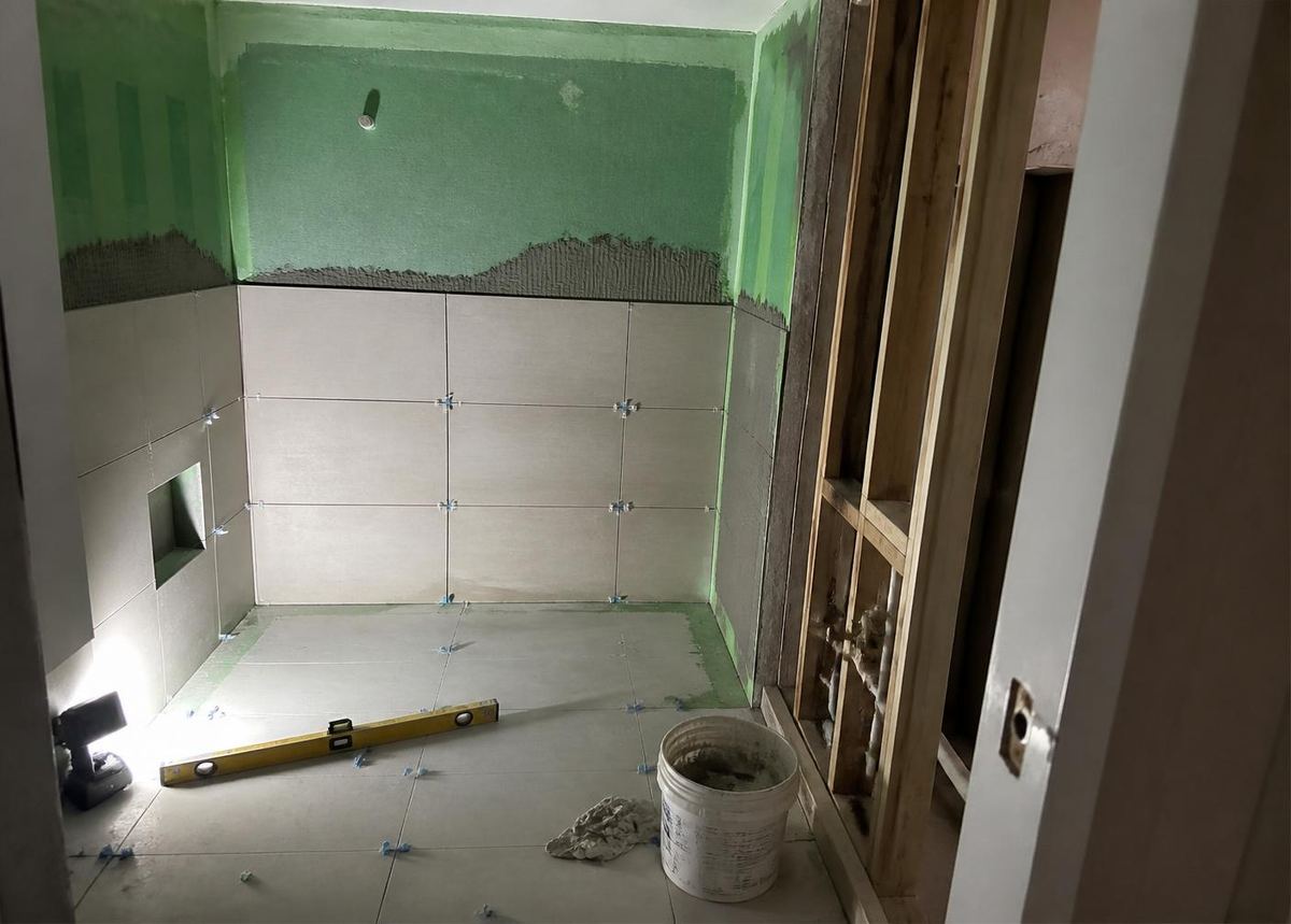 A small bathroom mid-renovation with waterproofing applied and wall tiles half laid.